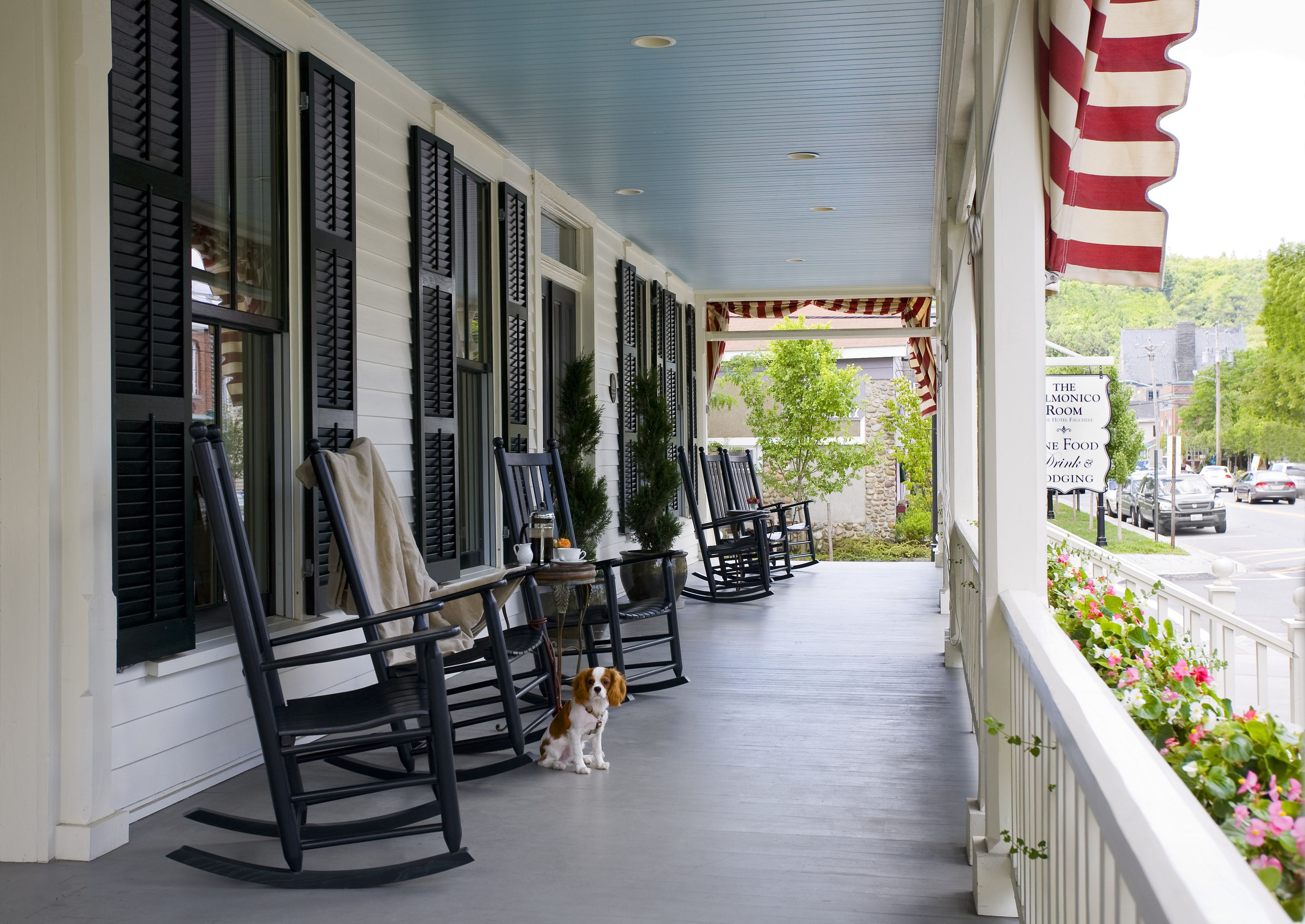 A porch with rocking chairs, a dog, and an American flag.
