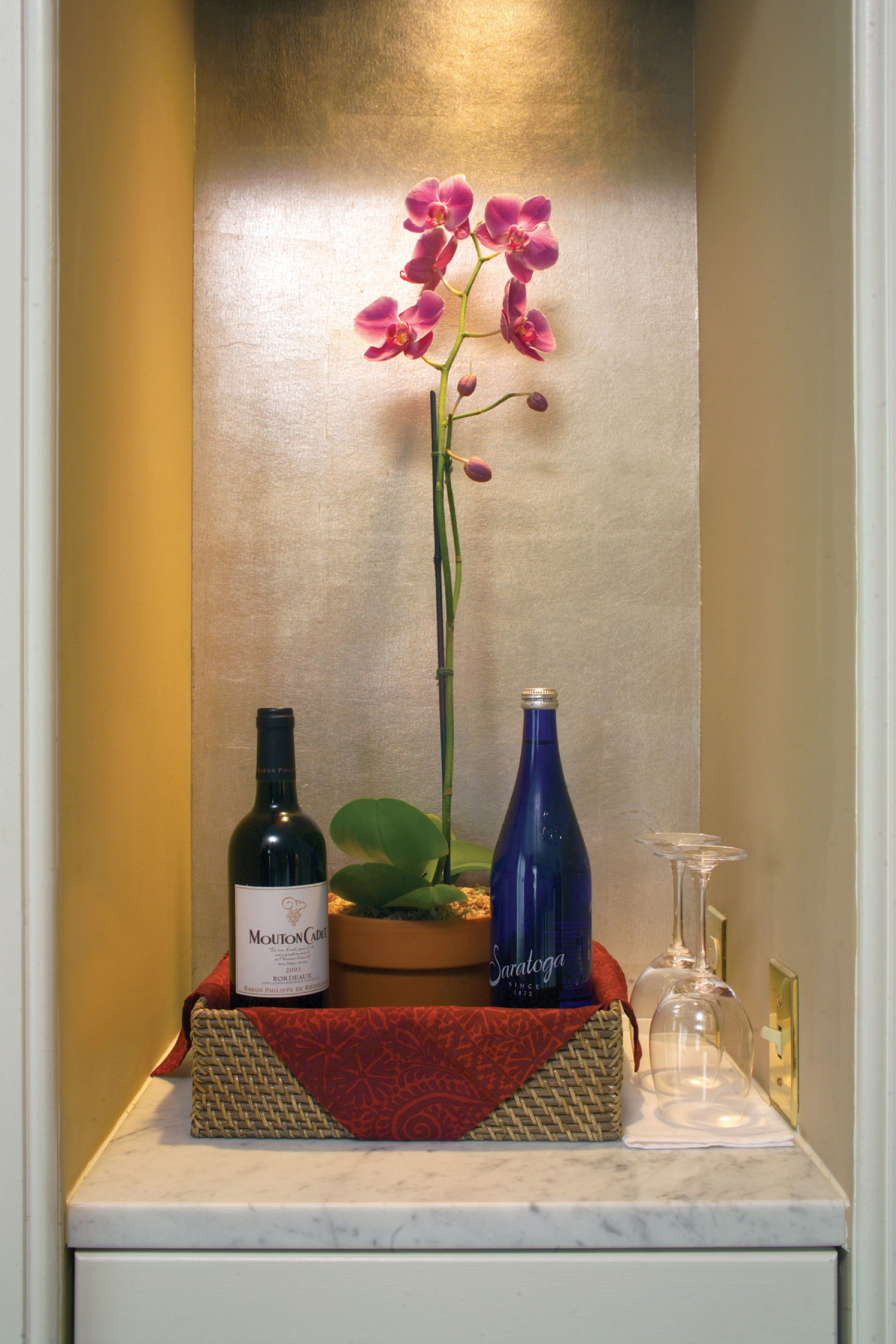 A marble countertop with a bottle of Mouton Cadre, a blue bottle, and a glass.