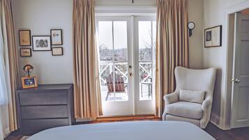 A bedroom with a large bed, a chair, a dresser, and a balcony with a view.