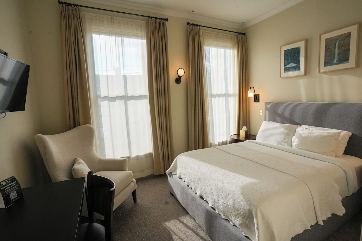 A hotel room with a bed, a chair, a desk, a TV, and curtains.