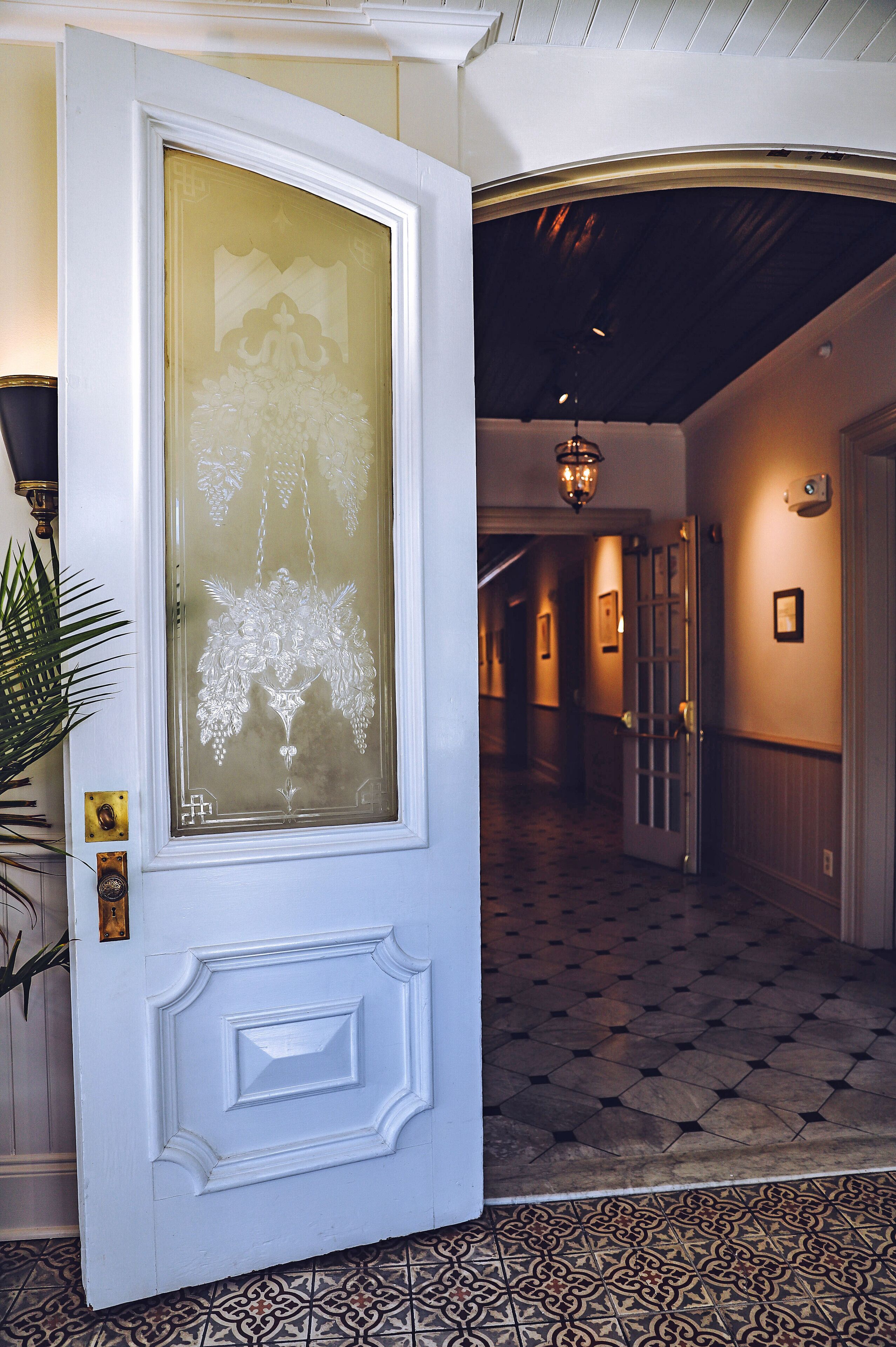 A hallway with a patterned floor, a white door with a frosted glass panel, and a hanging light fixture.