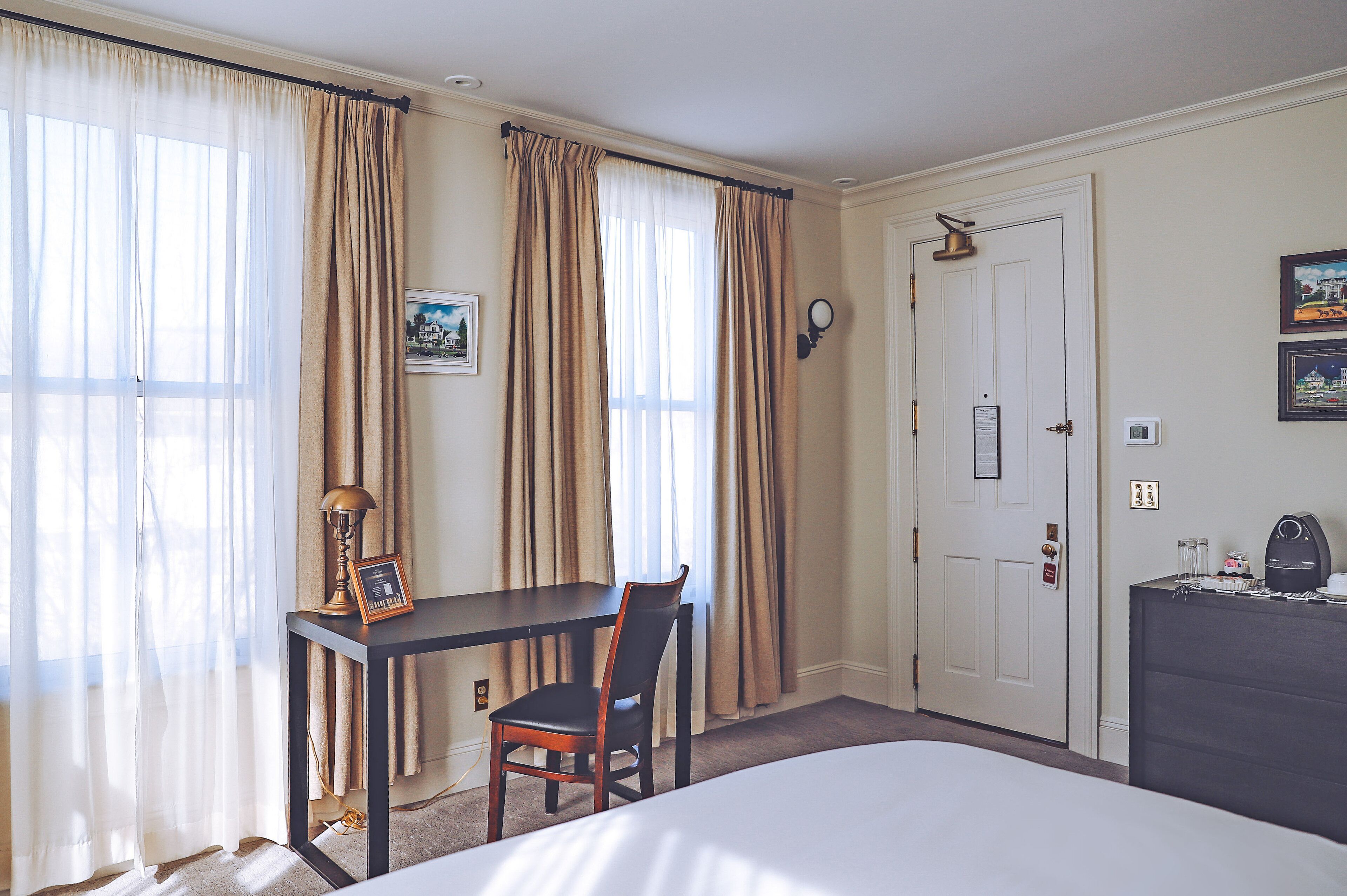 Una habitación de hotel con cama, escritorio con silla, puerta y cortinas.