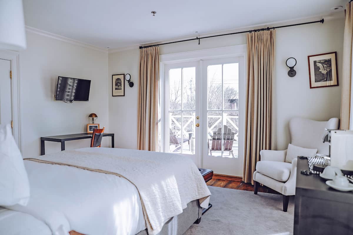 A bedroom with a bed, a desk, a chair, a TV, and a view of the outdoors.