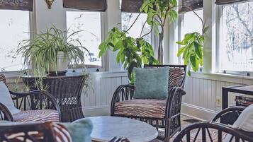 A cozy indoor seating area with wicker furniture, a large potted plant, and patterned floor tiles.