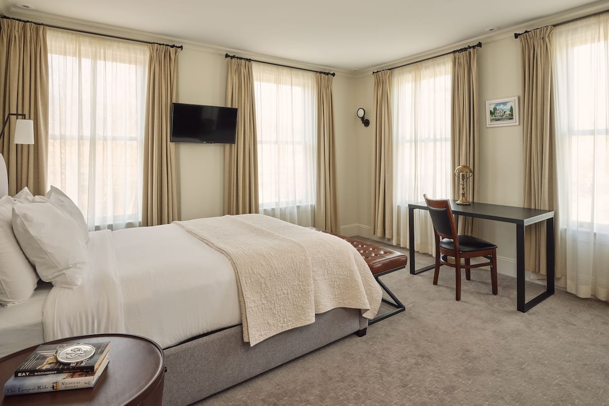 A hotel room with a bed, desk, chair, and a flat-screen TV.
