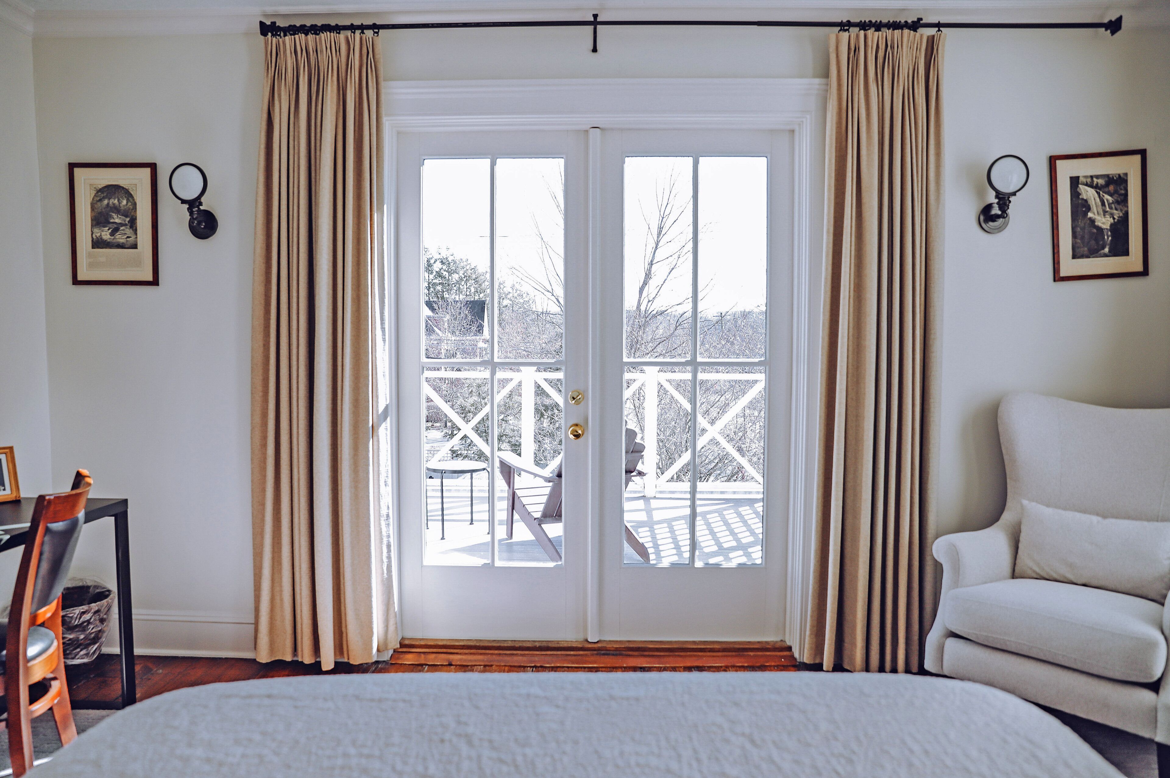 A bedroom with a large bed, a chair, a desk, and a view of an outdoor deck through a set of French doors.