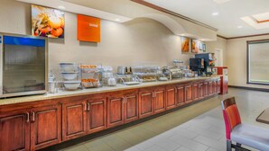 Uma mesa de buffet com diversas estações de comida, uma máquina de café e um refrigerador.