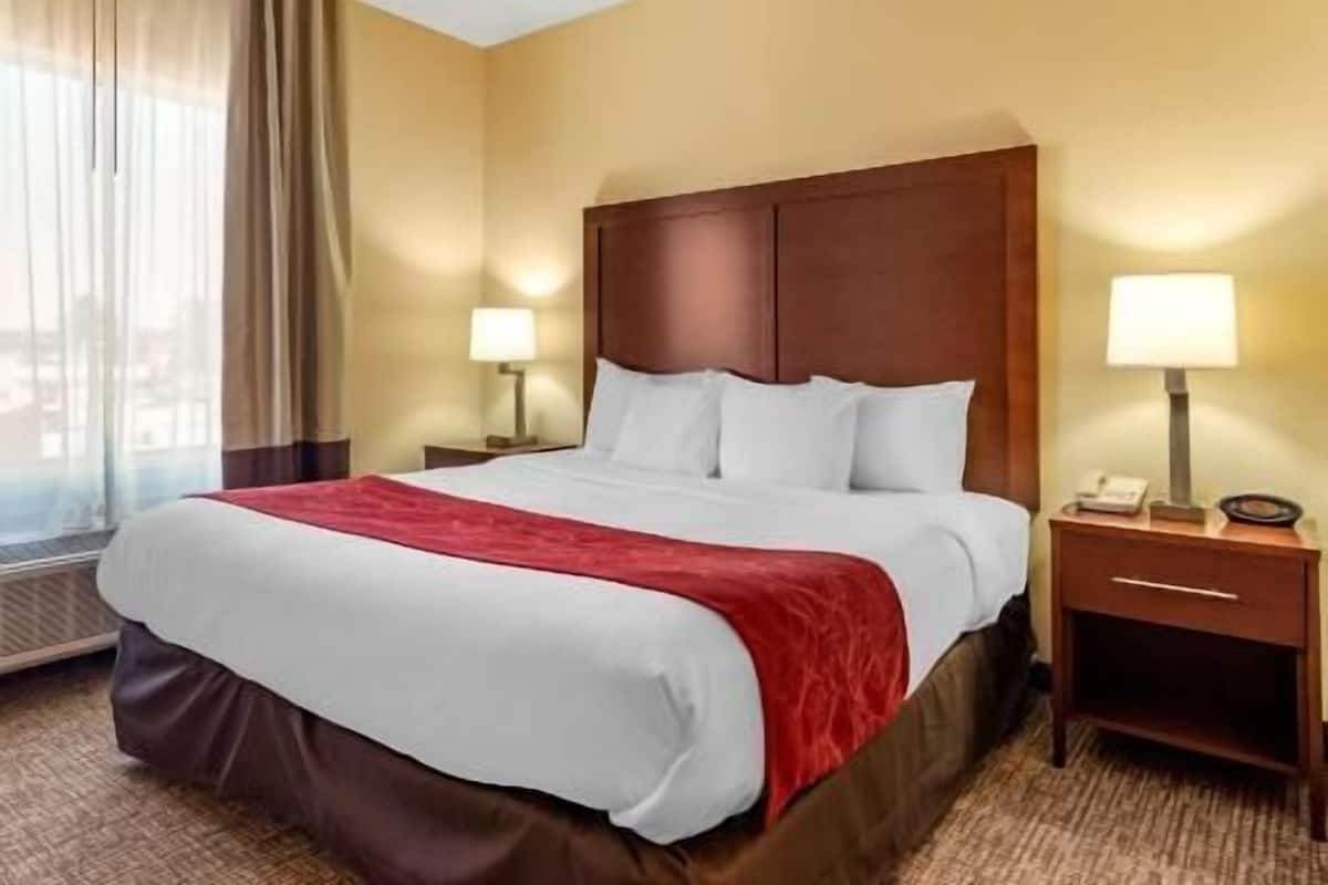 Una habitación de hotel con una cama grande, dos mesitas de noche y una ventana con cortinas.