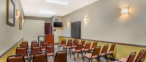 Une salle de conférence avec des rangées de chaises, un téléviseur à écran plat fixé au mur et des luminaires fixés au mur.
