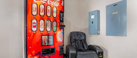A Coca-Cola vending machine with various drink options, a massage chair, and electrical panels on the wall.
