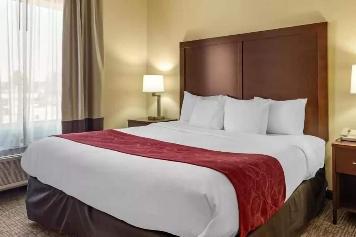 Habitación de hotel con una cama grande, dos mesitas de noche, una ventana con cortinas y un teléfono en la pared.