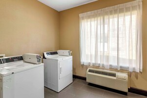 Un lavadero con dos lavadoras y una secadora, una ventana con cortinas translúcidas y un aire acondicionado de pared.
