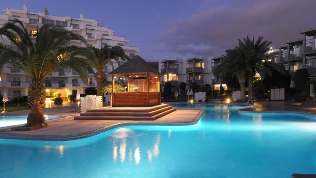 A swimming pool with a wooden gazebo, palm trees, and modern apartment buildings in the background. - Apartamentos HG Tenerife Sur (Arona)