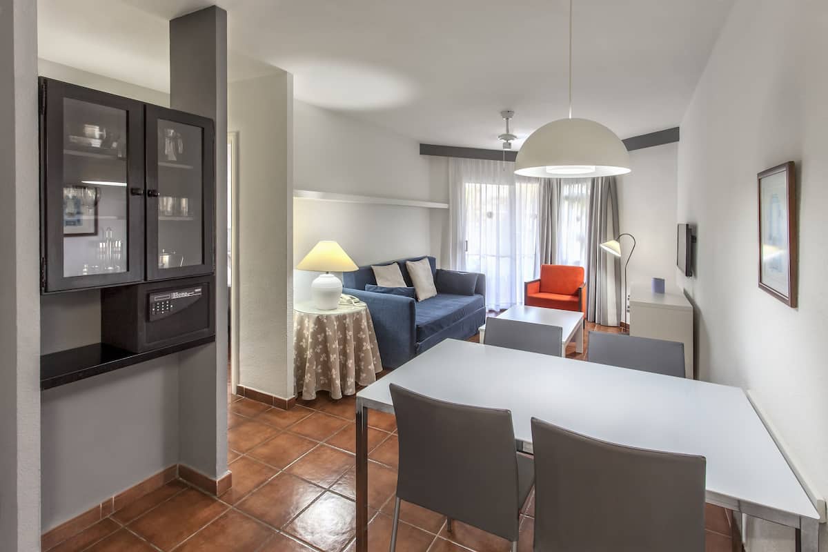 A modern living room with a sofa, a dining table, and a kitchen area with cabinets.