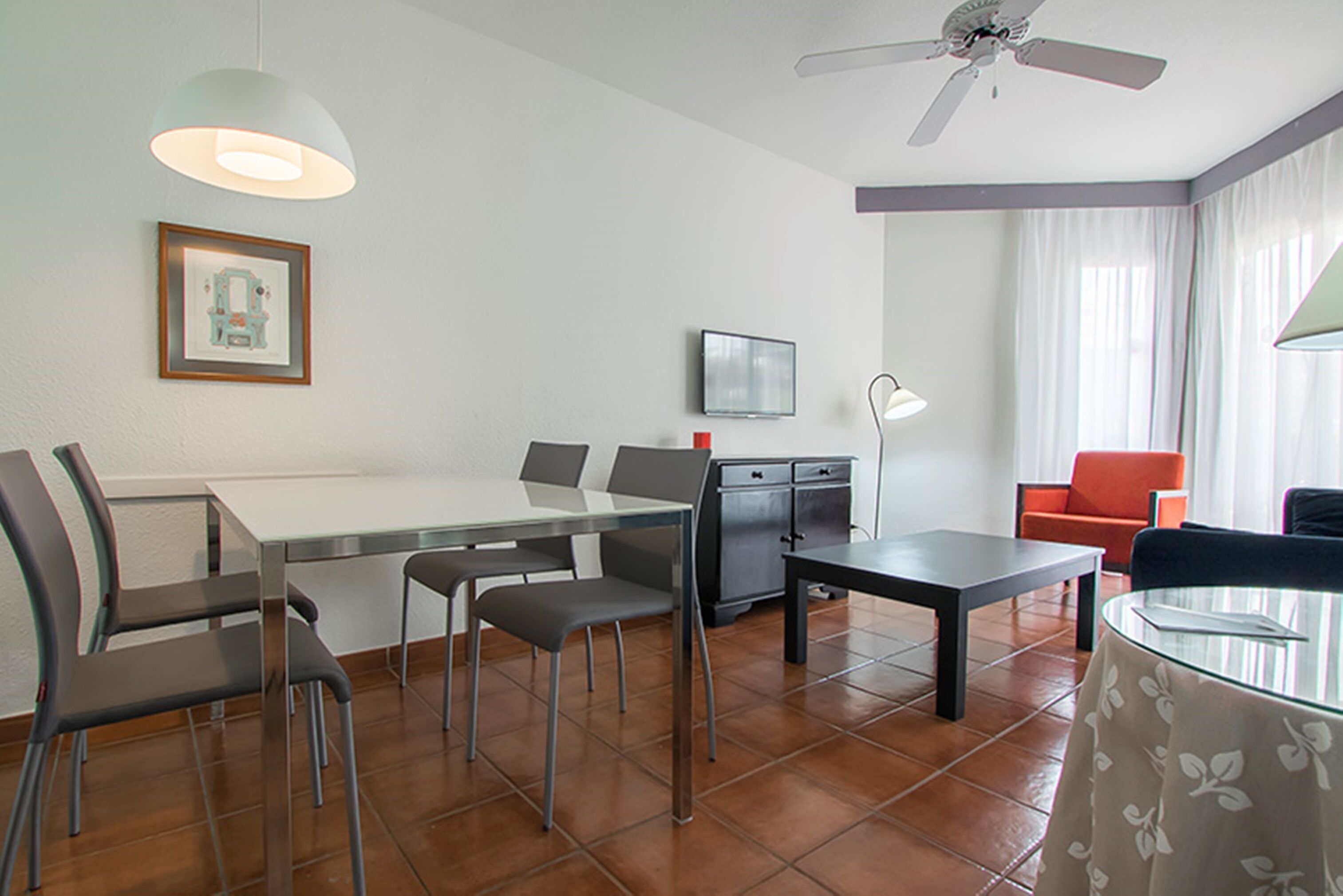 A modern living room with a dining area, a ceiling fan, a flat-screen TV, and a framed picture on the wall.