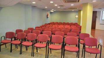 Une salle de conférence avec des rangées de chaises rouges et un extincteur accroché au mur.