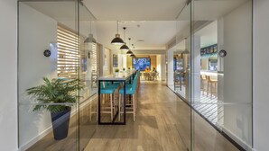 A modern interior with a glass partition, wooden flooring, and a bar area with blue chairs. - Apartamentos HG Lomo Blanco (Tías)
