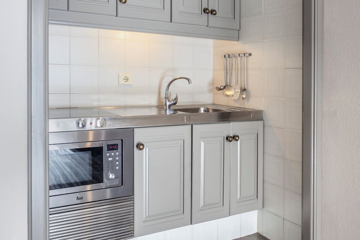 A compact kitchen with grey cabinets, a stainless steel oven, and a sink.