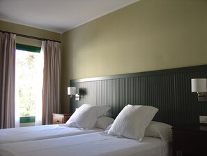 A hotel room with two beds, a nightstand, a lamp, and a window with curtains. - Apartamentos HG Lomo Blanco (Tías)