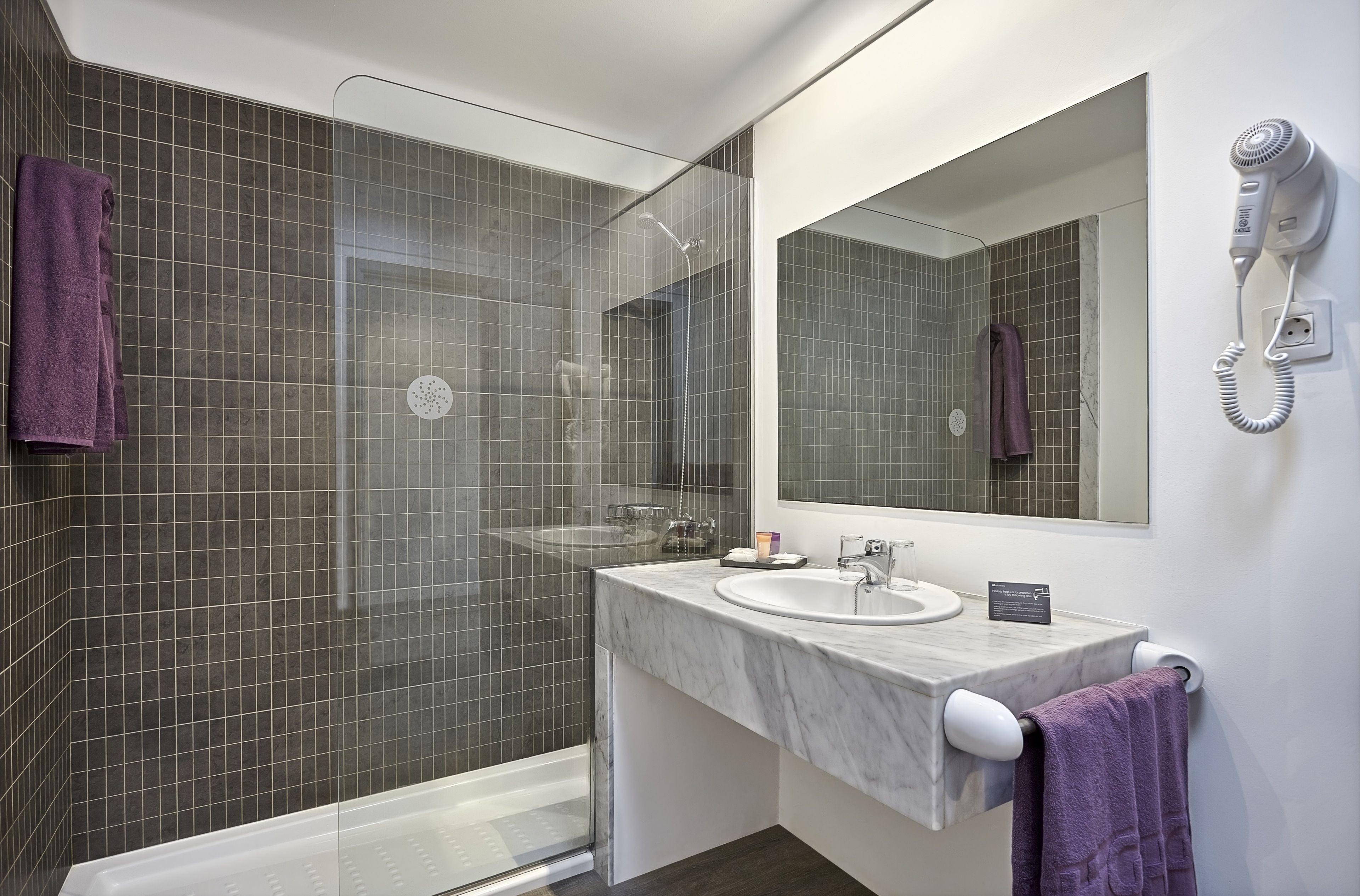 Une salle de bain moderne dotée d’une douche à parois de verre, d’un lavabo en marbre et d’un sèche-cheveux fixé au mur.