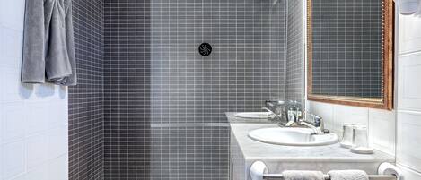 A modern bathroom with a bathtub, two sinks, a bidet, and a large mirror.