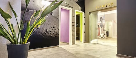 A modern fitness center with a large plant in the lobby, a purple wall, and a sign that reads "FITNESS".