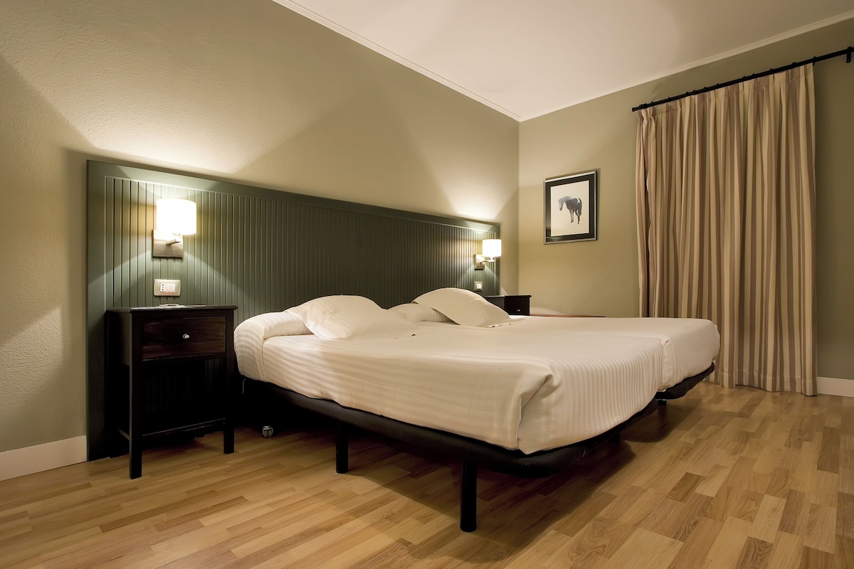 A neatly arranged bedroom with a bed, bedside tables, a wall-mounted light, and a curtain.