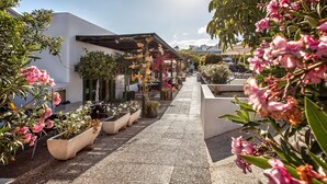 A pathway lined with potted plants and flowers leading to a covered area with a pergola. - Apartamentos HG Lomo Blanco (Tías)