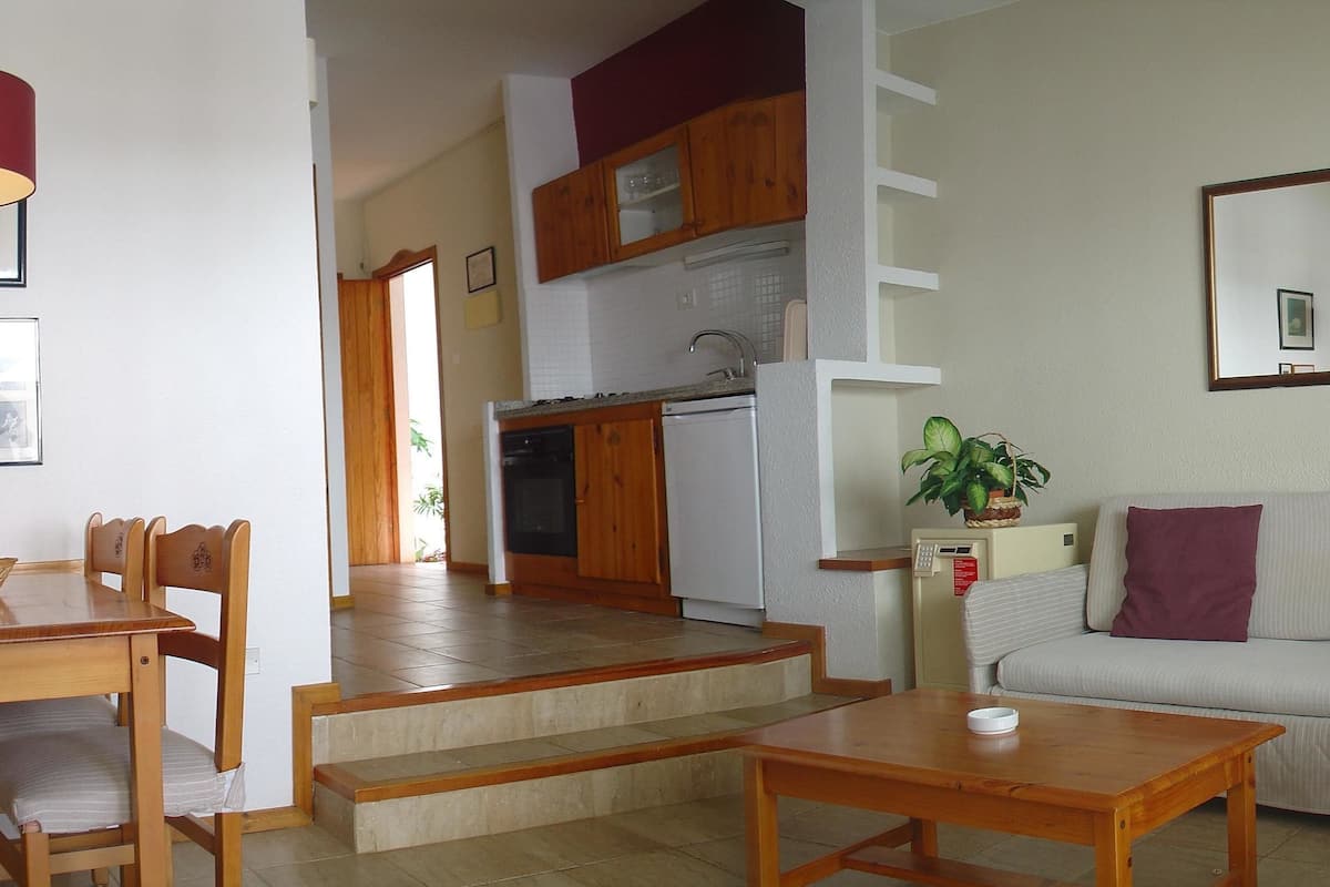 A living room with a sofa, a dining table with chairs, a coffee table, a kitchen area with a refrigerator, and a staircase.