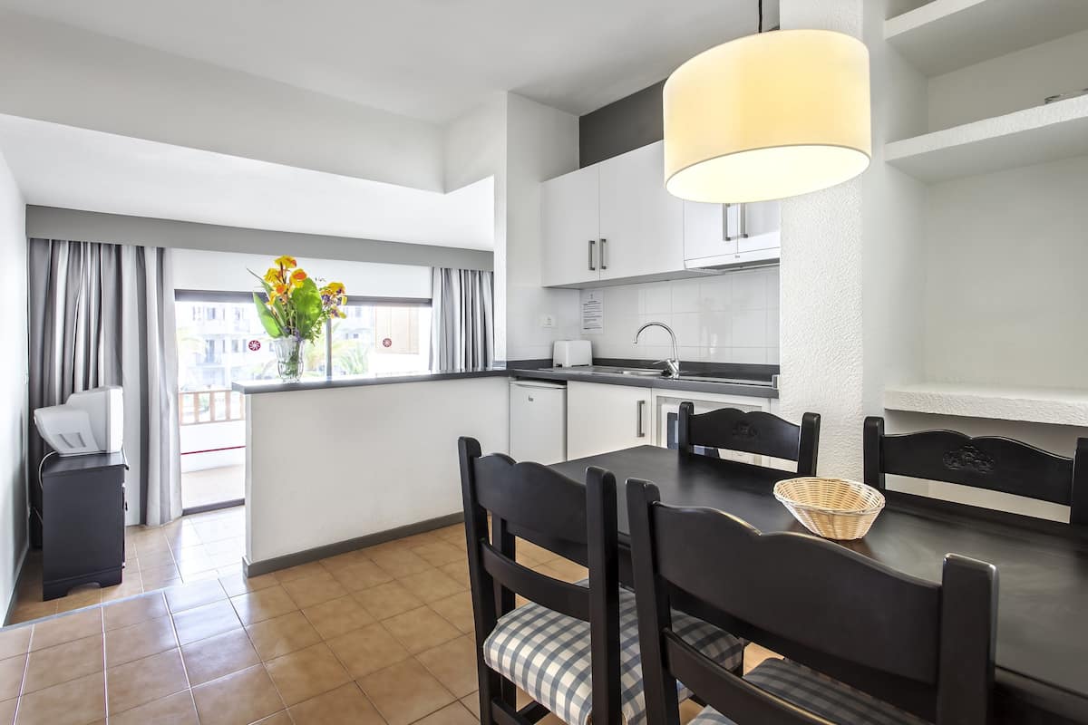 A modern kitchen with a dining area, featuring a black dining table, chairs, and a hanging light fixture.