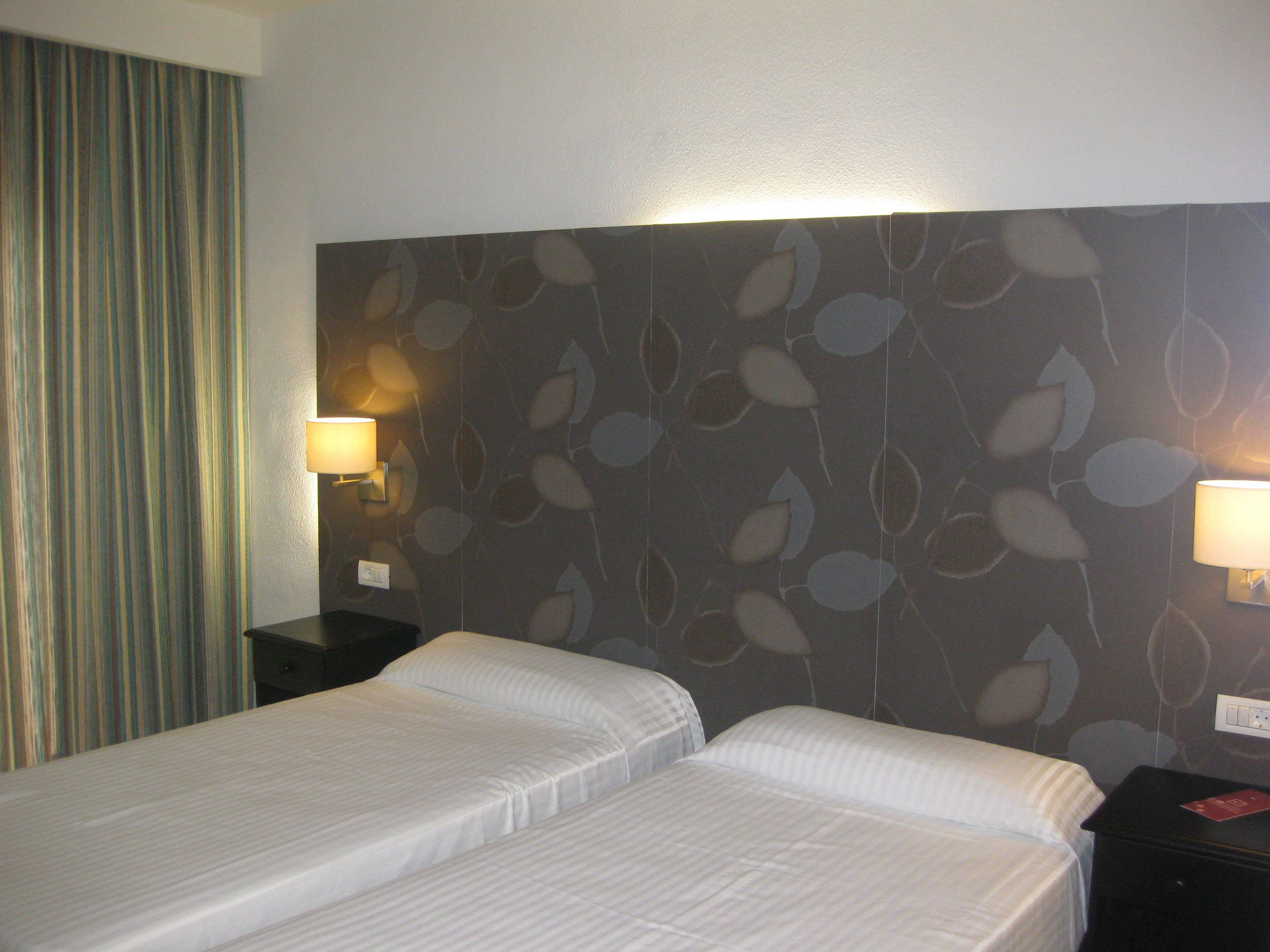 A hotel room with two beds, a curtain, and wall-mounted lamps.