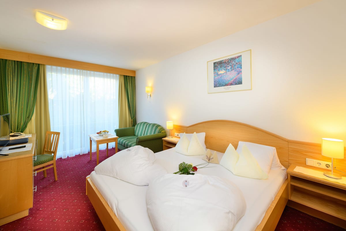 A hotel room with a bed, a desk, a chair, a lamp, and a painting on the wall.