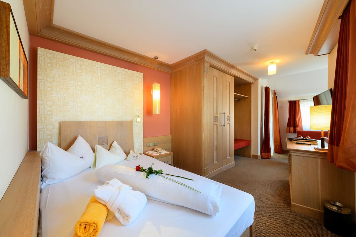 A hotel room with a large bed, a wooden wardrobe, a desk with a lamp, and a television.