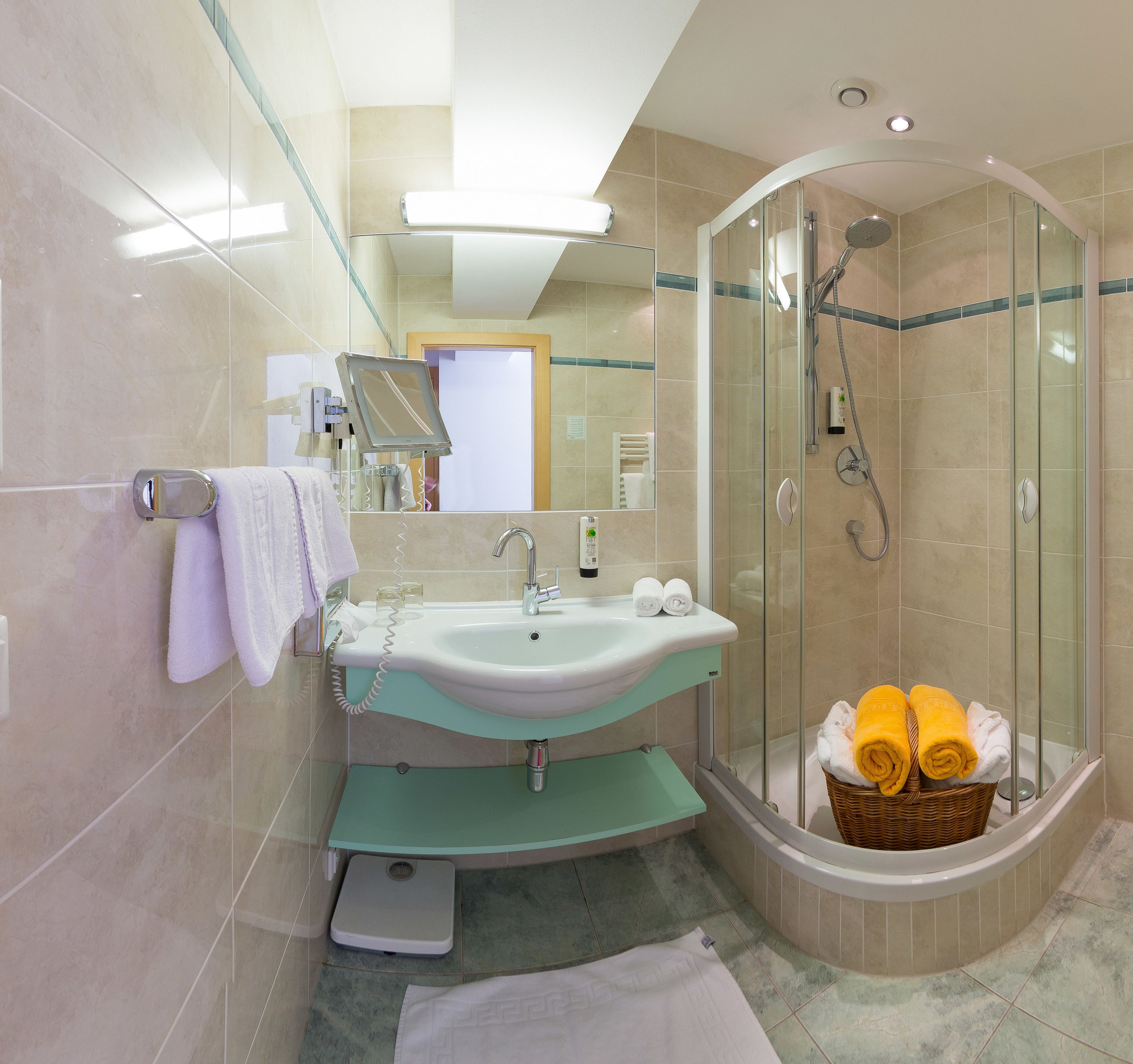 Un baño moderno con ducha de vidrio, un lavamanos con espejo y tocador con toallero.