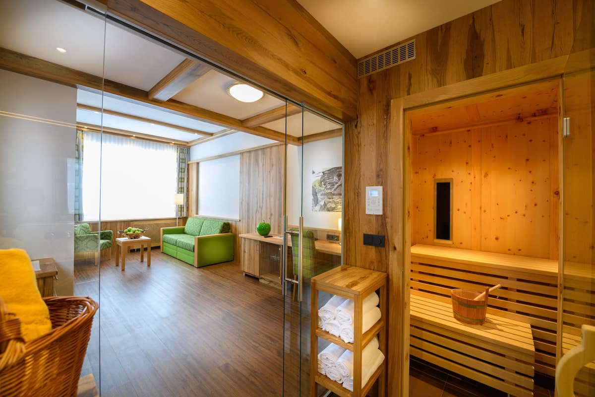 A modern room with wooden walls, a glass partition, a green sofa, a wooden bench, and a sauna area.