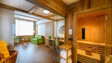 A modern room with wooden walls, a glass partition, a green sofa, a wooden bench, and a sauna area.