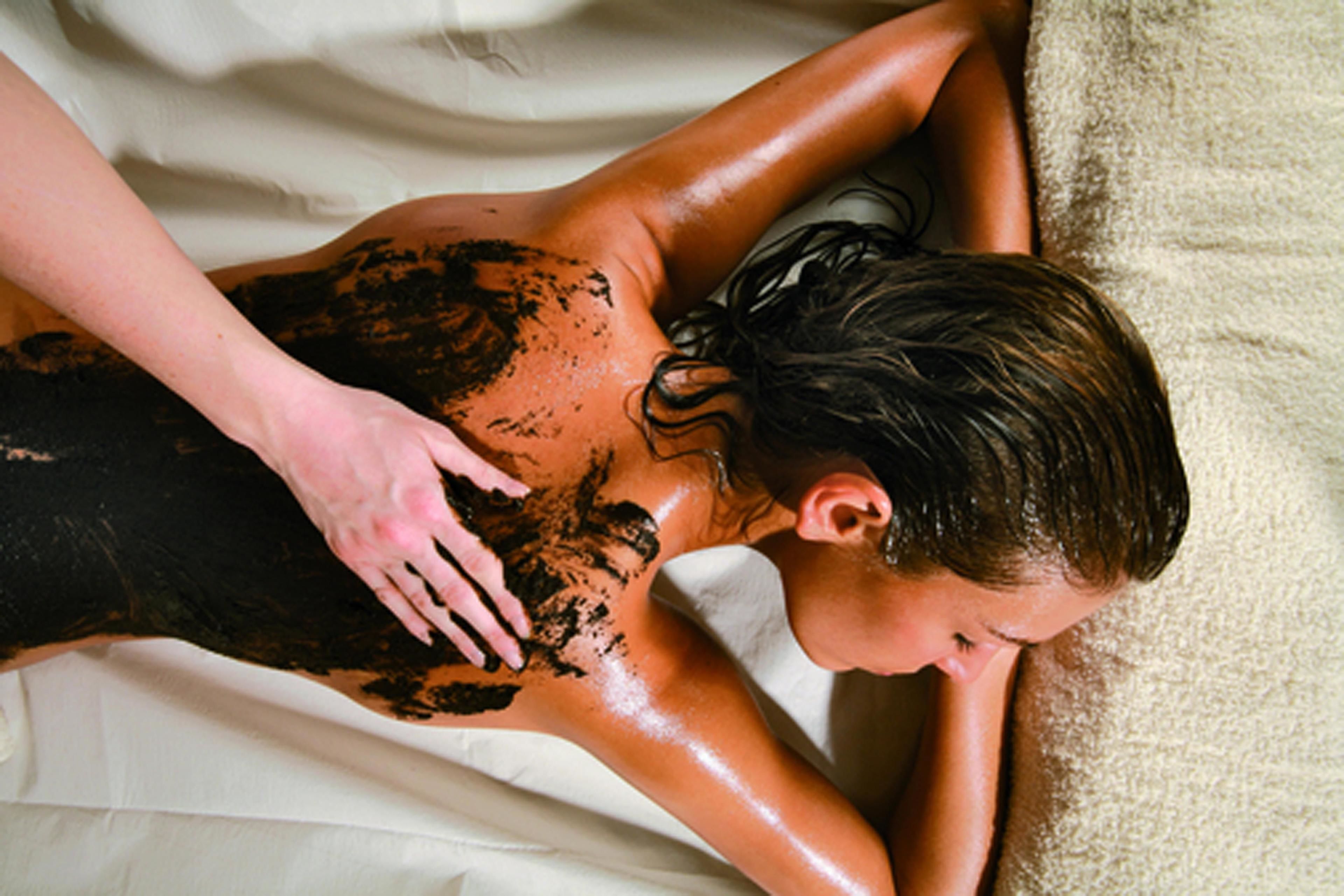 Iemand ontvangt een rugmassage op een bed met een wit laken.