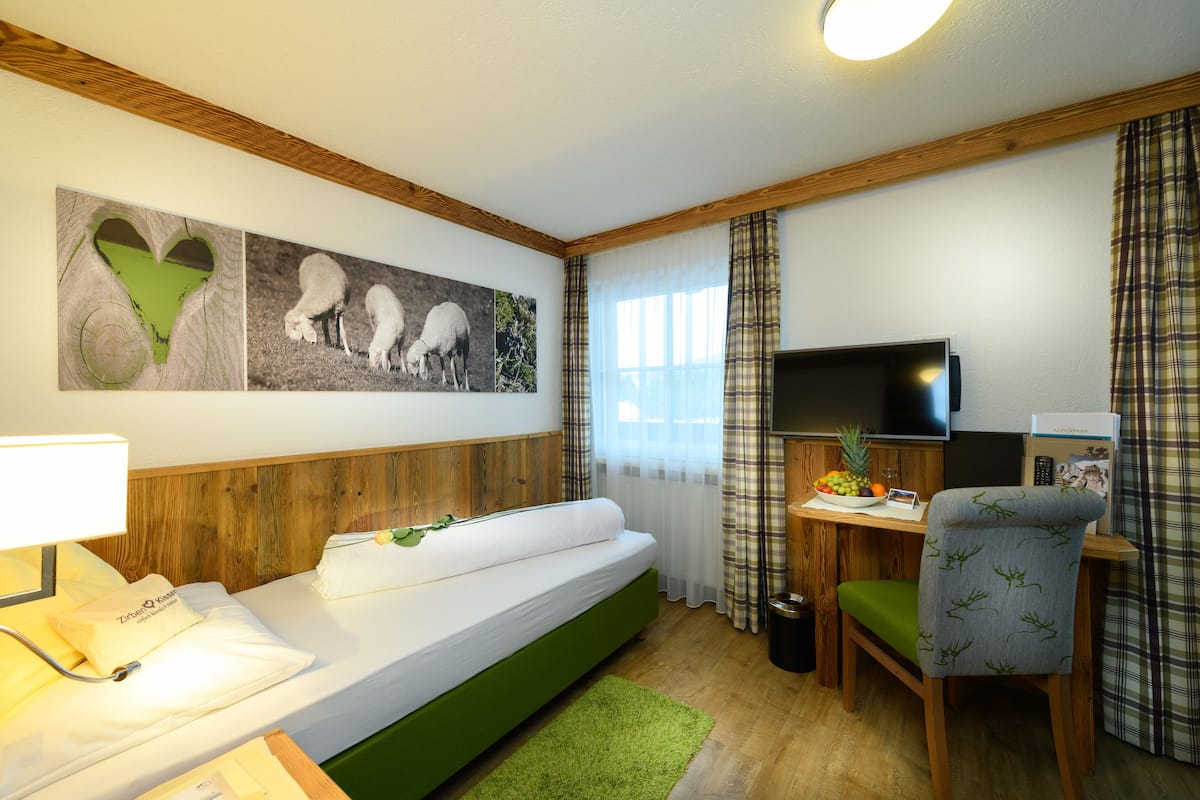 A room with a bed, a desk with a TV, a chair, and a wall with artwork.