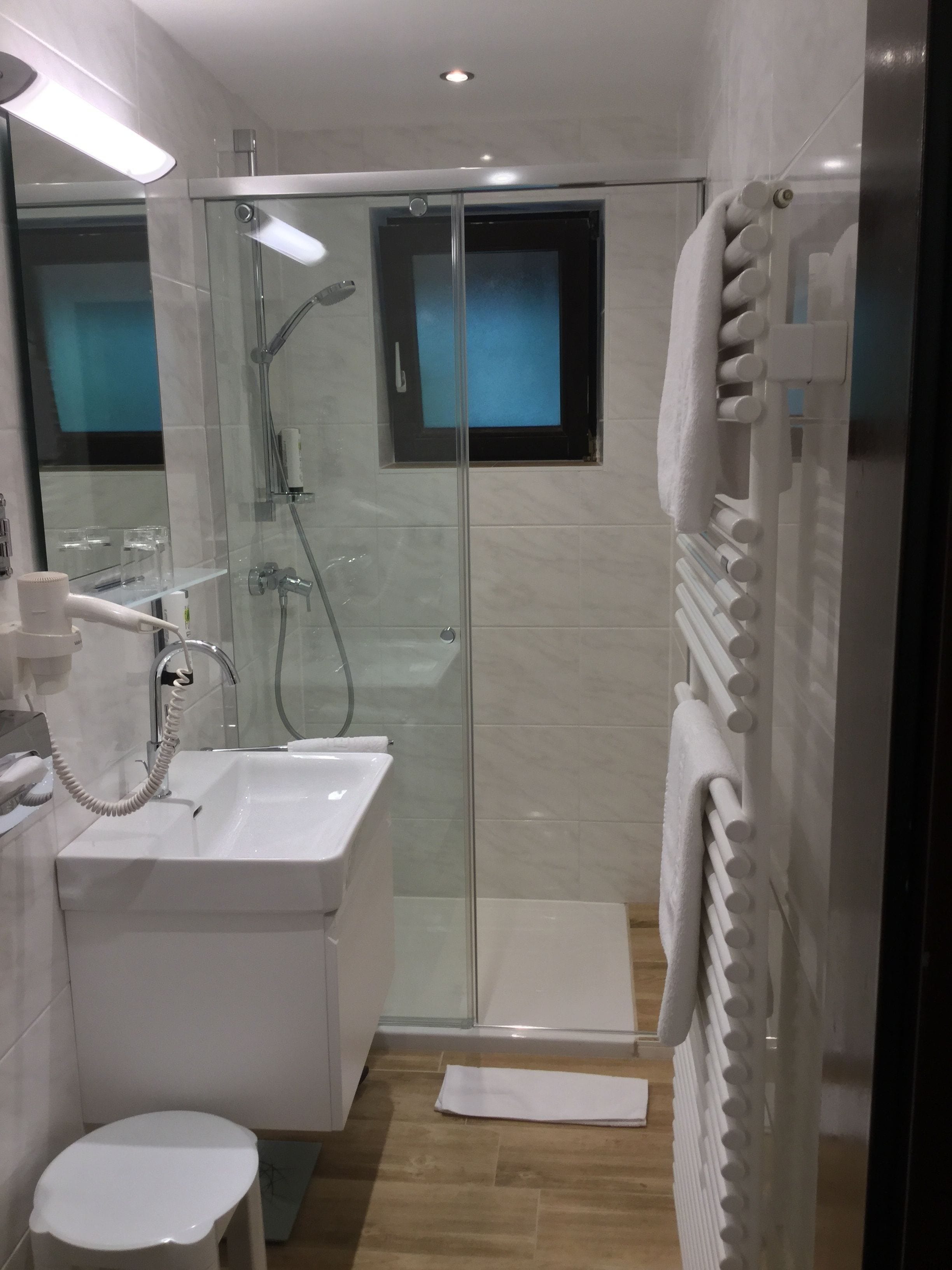 A modern bathroom with a glass-enclosed shower, a white sink, and a towel rack.