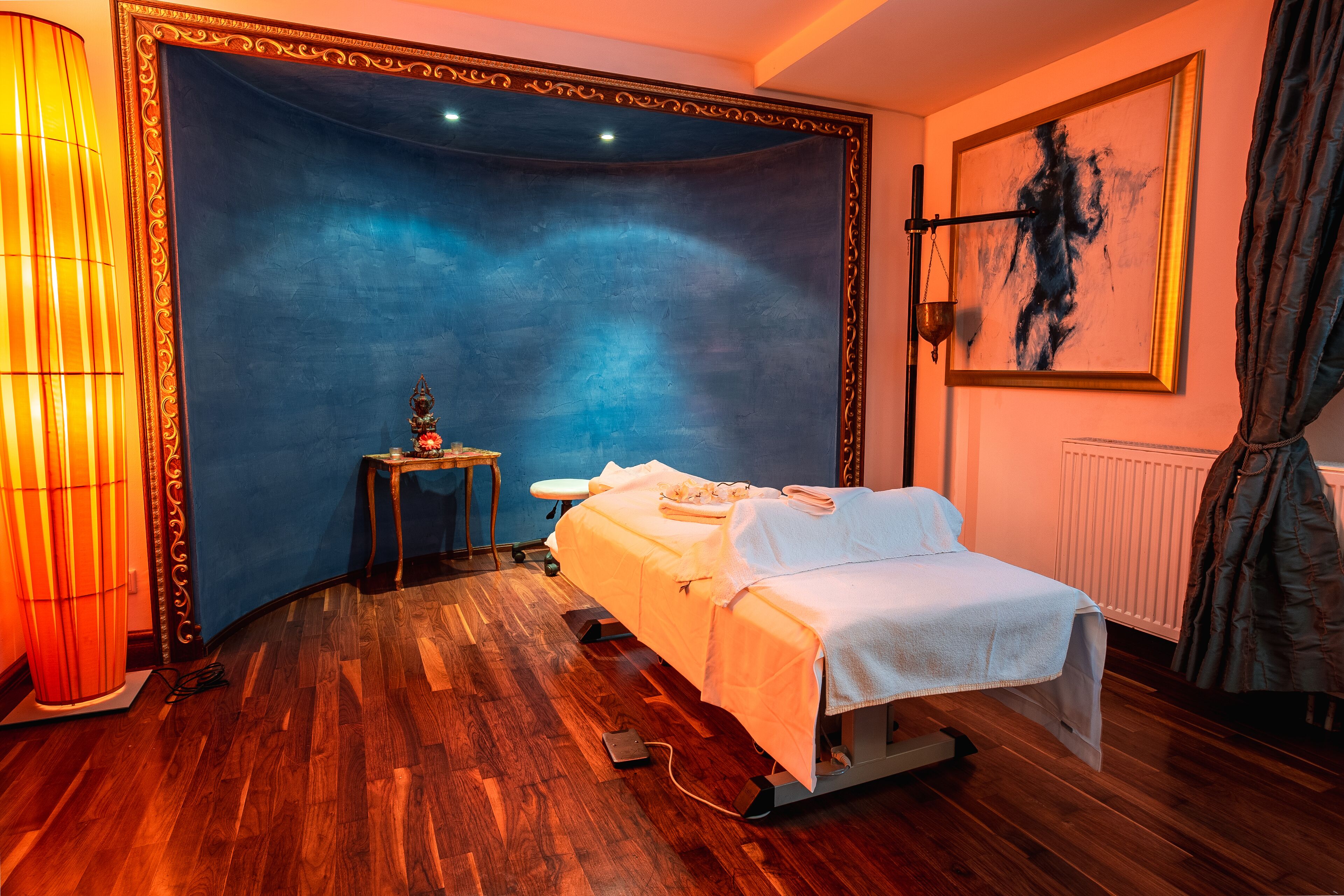 A room with a massage table, a lamp, and a painting on the wall.