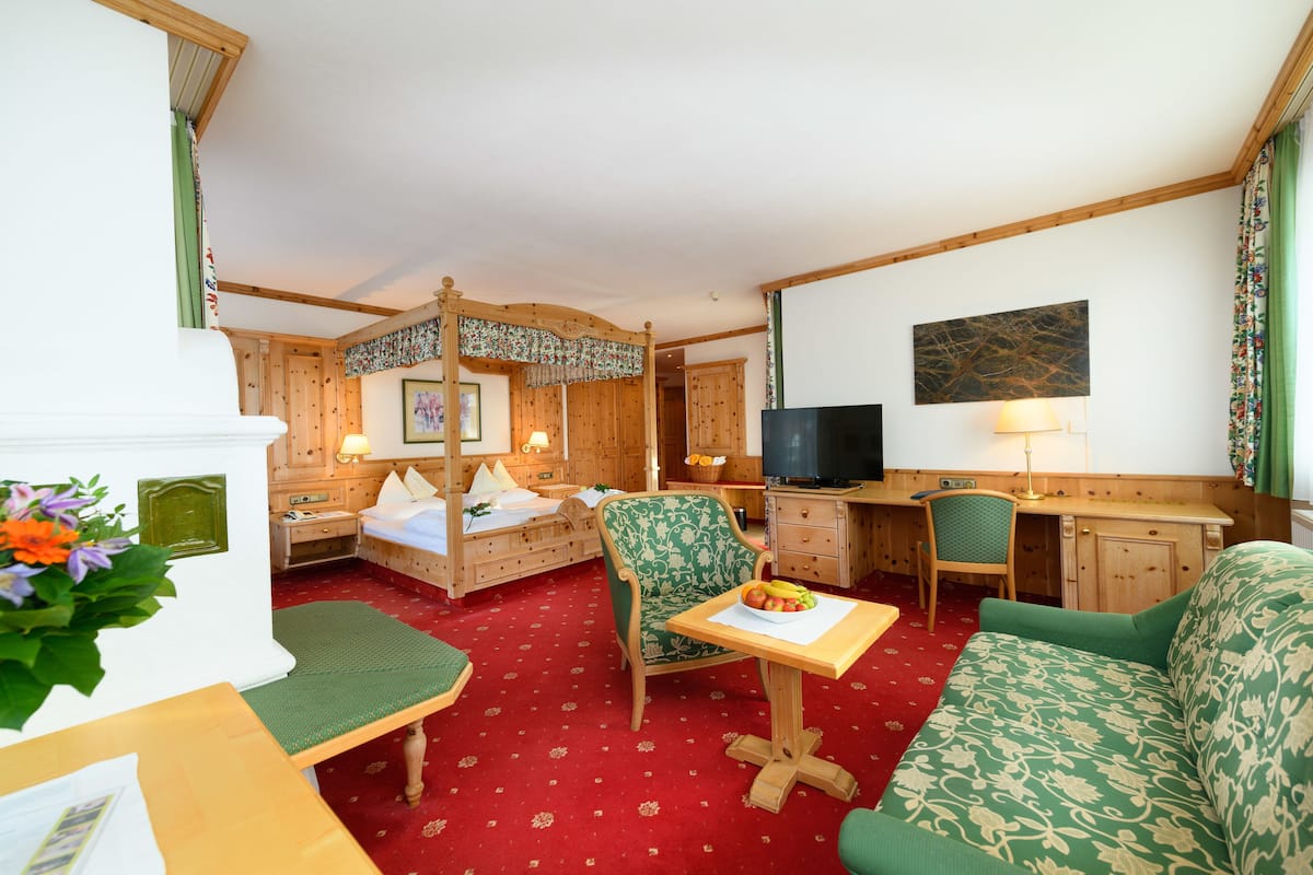 A hotel room with a wooden bed, a desk, a green sofa, and a television.