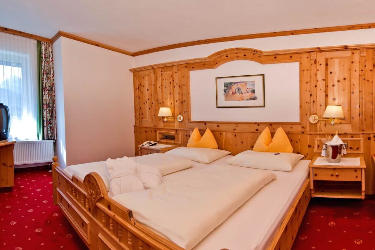 A hotel room with a wooden bed, two bedside tables with lamps, a painting on the wall, and a window with curtains.