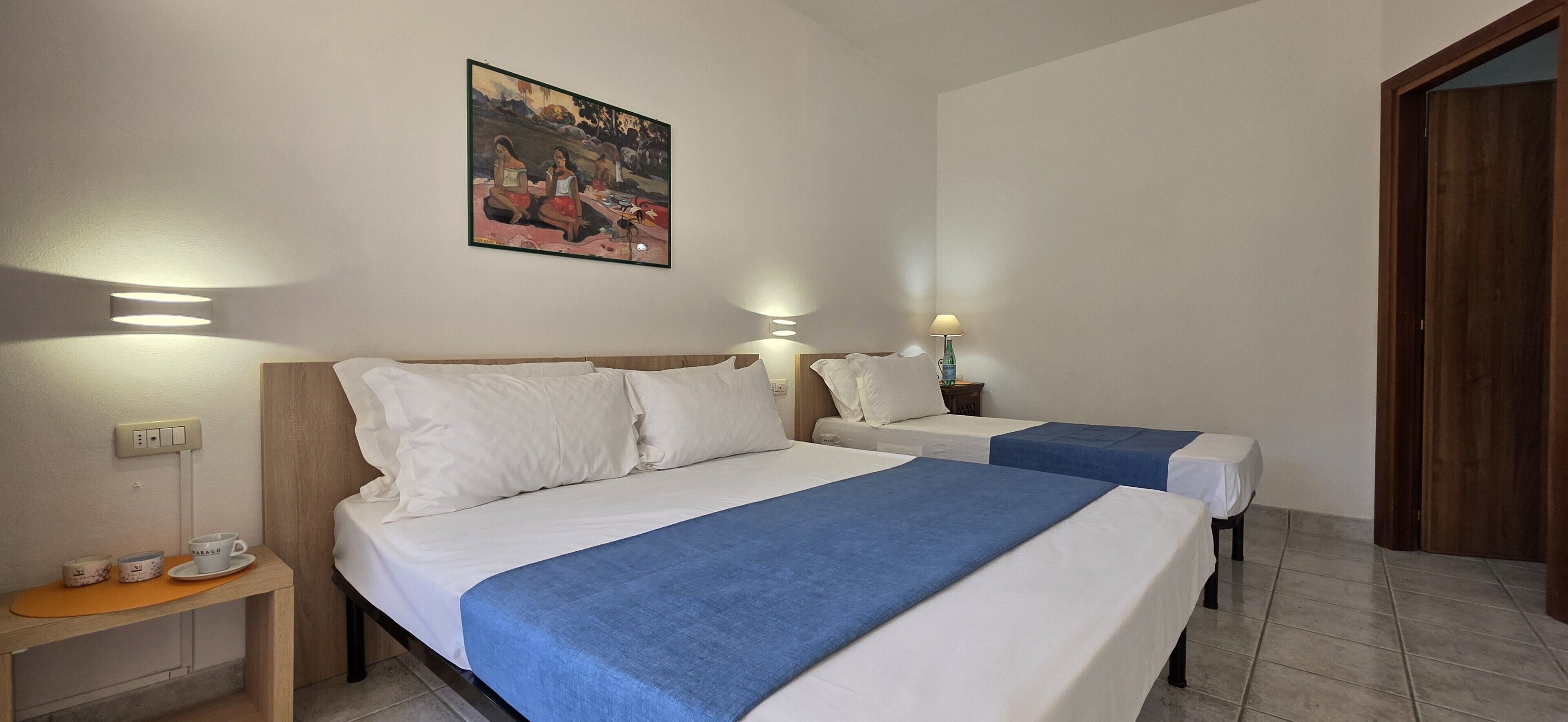 Una habitación de hotel con dos camas, un cuadro en la pared, lámparas de noche, una mesita con una taza y un plato, y una puerta de madera.