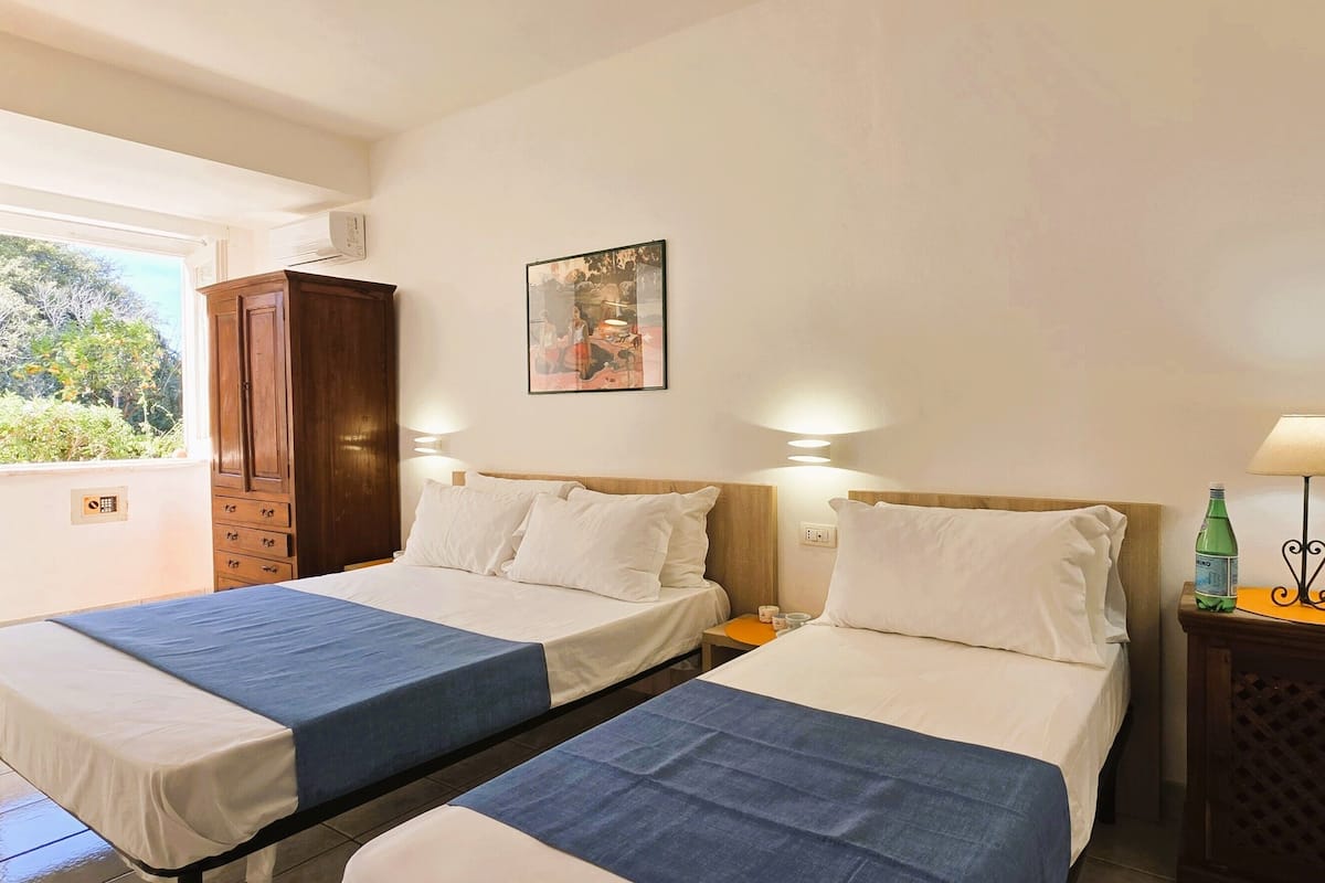 Een hotelkamer met twee bedden, een houten garderobe, een klein tafeltje met een lamp en een schilderij aan de muur.