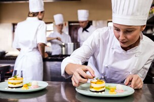Un chef preparando postres en una cocina profesional, con otros chefs al fondo.