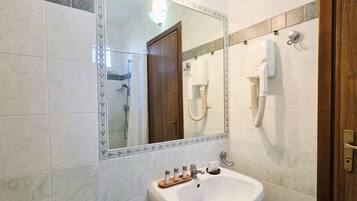 Une salle de bain équipée d’un lavabo, d’un miroir et de deux sèche-cheveux fixés au mur.