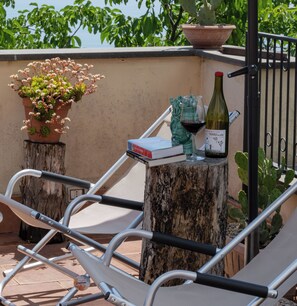 Une terrasse avec une chaise en métal, un pot de fleurs, une bouteille de vin et un livre.