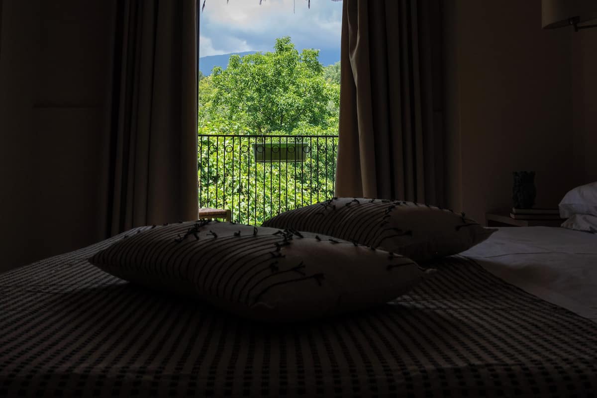 Une chambre à coucher avec un lit, deux oreillers, une table de chevet et une vue sur un balcon agrémenté de verdure.