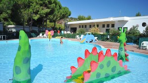 A swimming pool with inflatable dinosaur toys, a building with a white facade, and trees in the background.