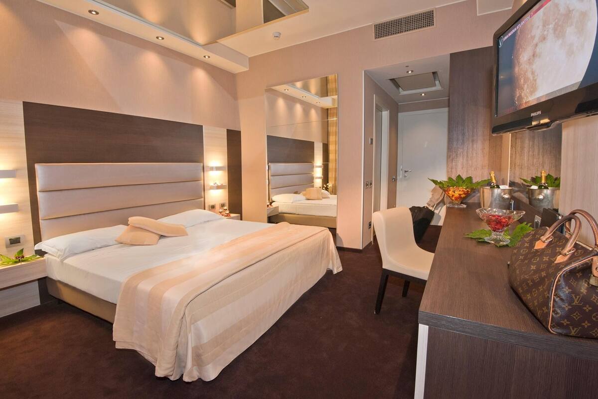 Ein Hotelzimmer mit einem großen Bett, einem Schreibtisch mit Stuhl, einem Fernseher und einer Minibar.